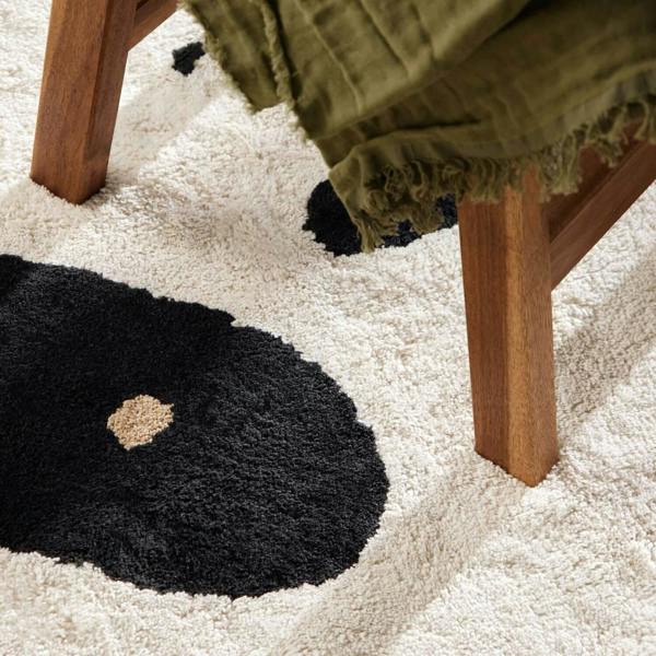 Close-up of a black rug with a beige center on a white carpet, next to a wooden chair.
