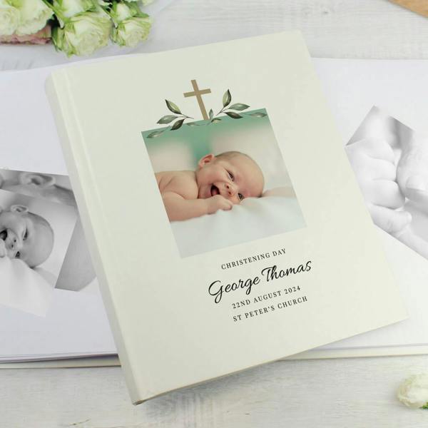 A satin-finish traditional photo album printed with a cross, leaves, a photo of a baby, and reading George Thomas Christening Day.
