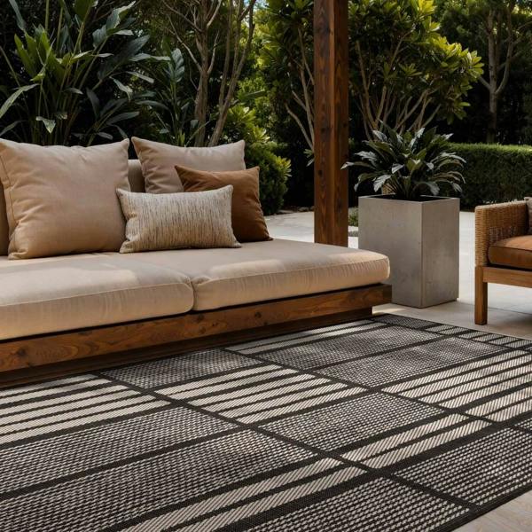 Outdoor seating area with a beige cushioned sofa and striped rug on a patio.