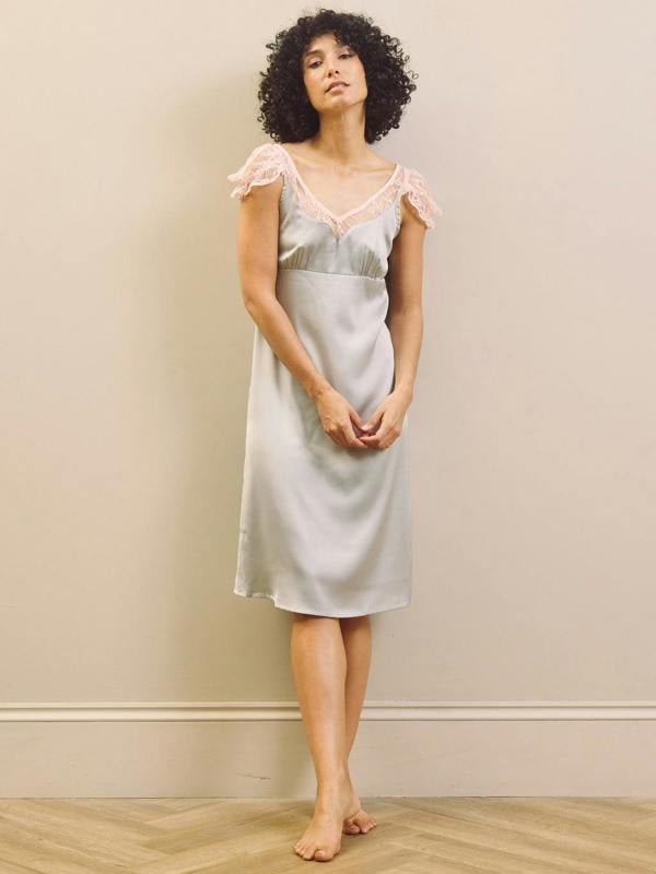 Woman wearing a light blue slip nightdress with lace trim against a beige wall.