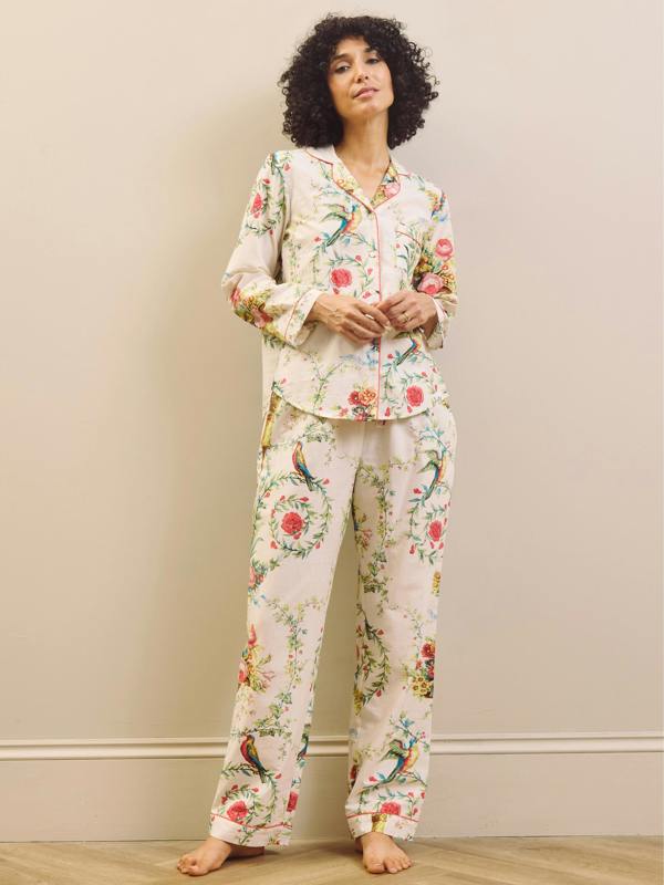 Model wears a white based floral print pyjama set against a beige wall. 