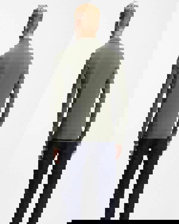 Man wearing a green long-sleeve polo shirt and dark pants on a white background