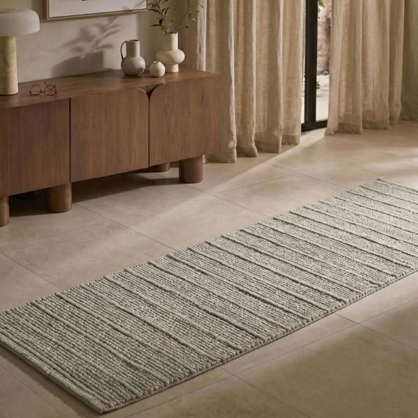 Long rectangular rug on a tiled floor with a wooden sideboard and curtains in the background.