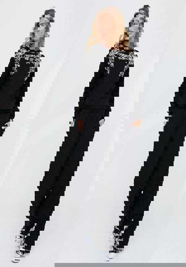 Woman wearing a black outfit with white embroidery on a white background