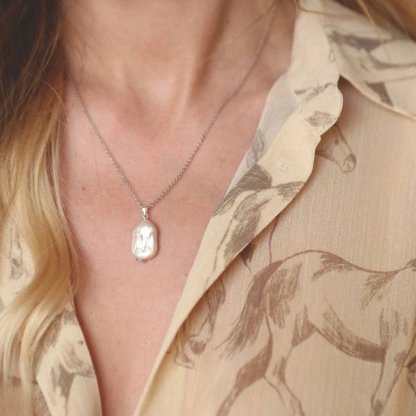 Model wearing a silver necklace with a rectangular baroque pearl pendant.