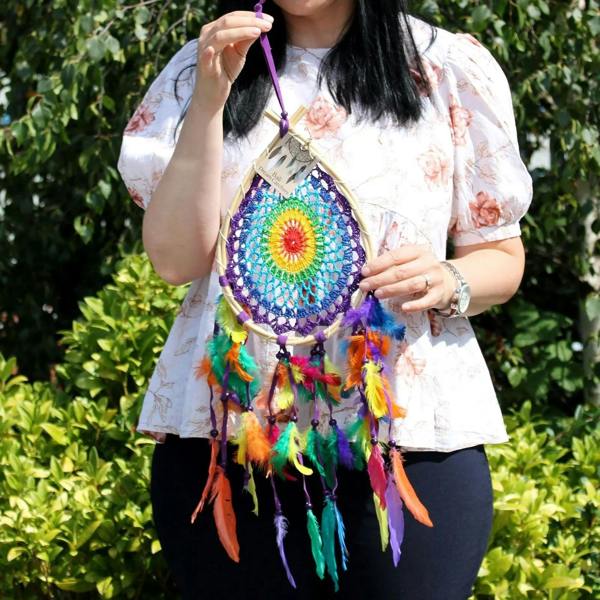 Teardrop dream catcher worn at chest, blue net with rainbow feathers and circular center design.