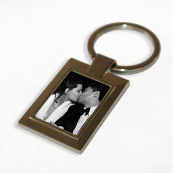 A rectangular silver-toned metal photo keyring featuring a black and white photo of a couple kissing, isolated on a clean white background.