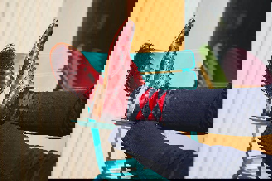 Person wearing red leather shoes and patterned socks sitting on a colorful chair.