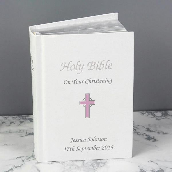 Personalised white leatherette Holy Bible with a small pink cross engraved with "Jessica Johnson" on a marbled surface.