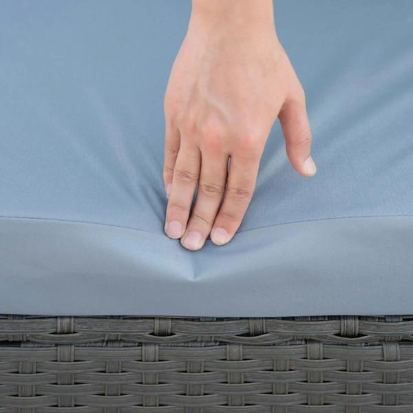 Dusty blue cushion being adjusted and smoothed by a hand on a rattan seat