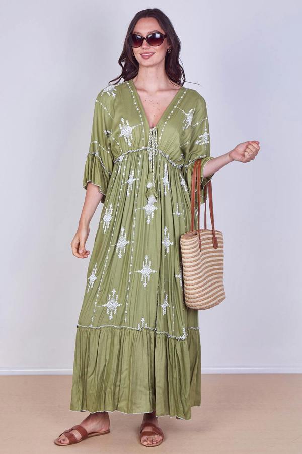 Woman wearing a green dress with white patterns, holding a straw bag against a white background