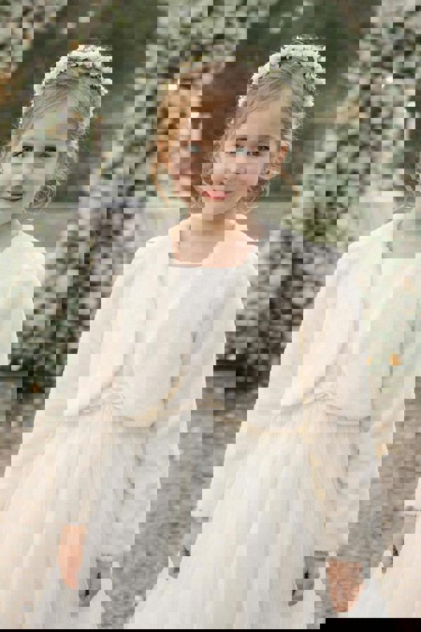 Young girl in a white dress with a fur shrug standing in front of floral decorations.