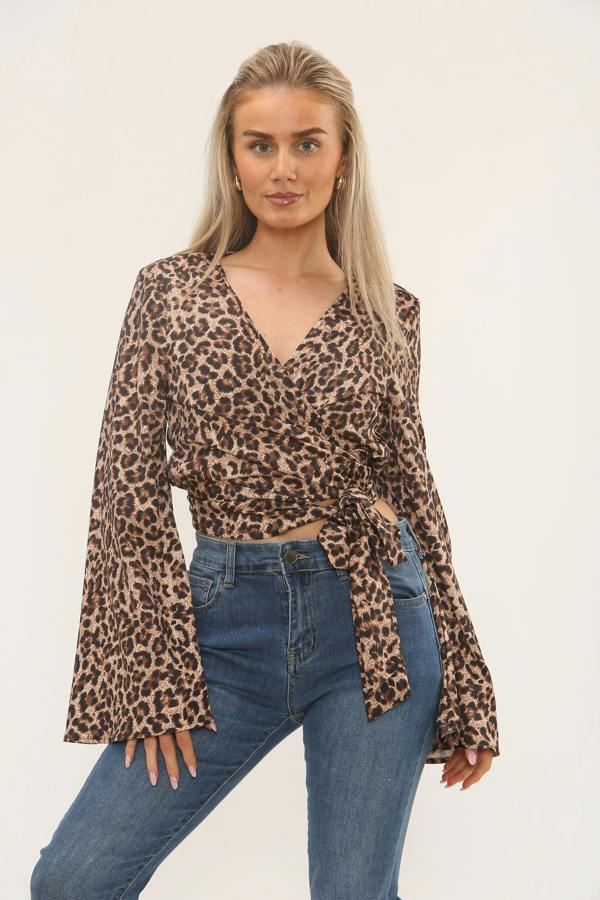 Woman wearing a leopard print satin wrap top with flared sleeves, paired with high-waisted blue jeans, posing against a plain background