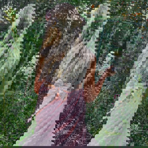 girl with headband and bouquet, standing in a garden.