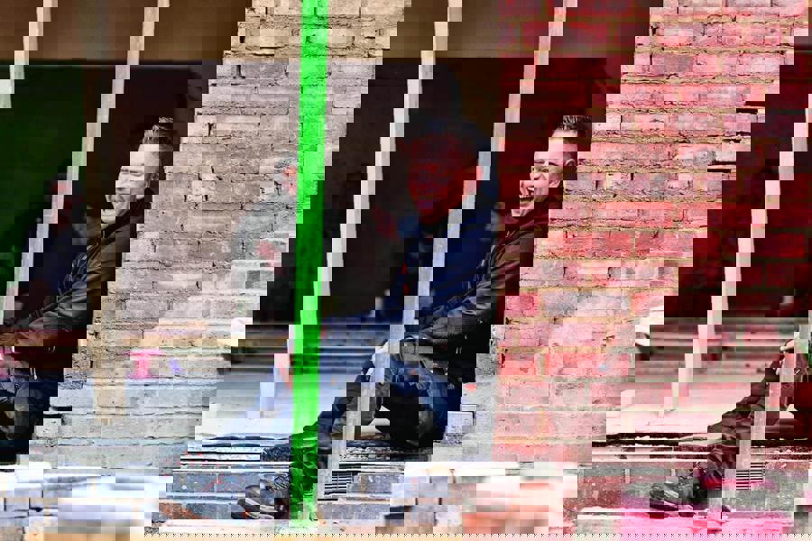 Scruffs Trade Flex Softshell Mens Zip Up Work Warm Jacket Coat, a man sitting at a construction site wearing a black softshell jacket with a zipper, suitable for work and outdoor activities.