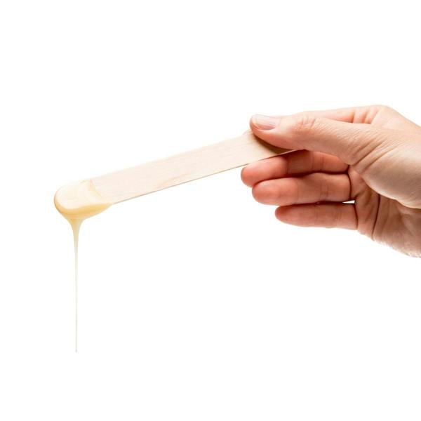 hand holding a spatula with melted wax dripping off it 