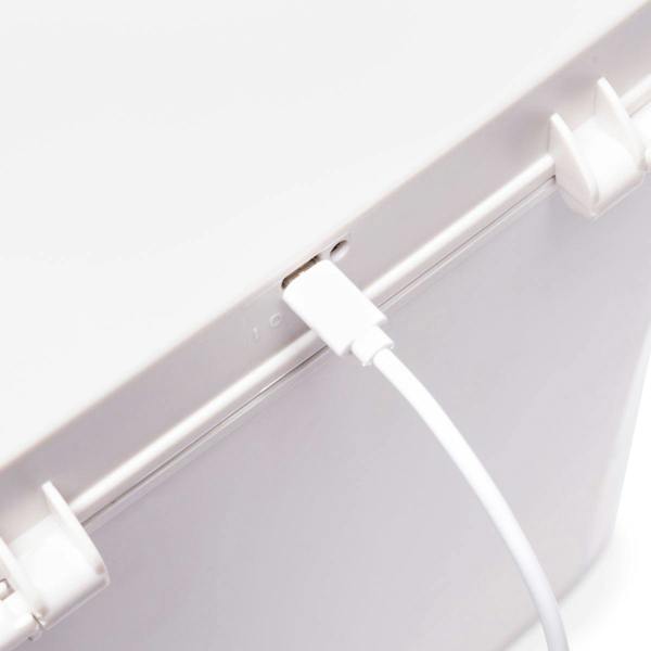 A close-up of a white USB cable plugged into the Ultimate Beauty Storage Box With Dimmable Mirror by Rio, a white plastic makeup organizer featuring latches on the lid.