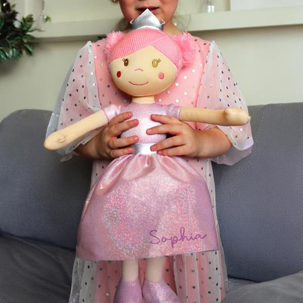 A young girl in a pink polka dot dress holding a personalised princess ballerina rag doll printed with the name Sophia.