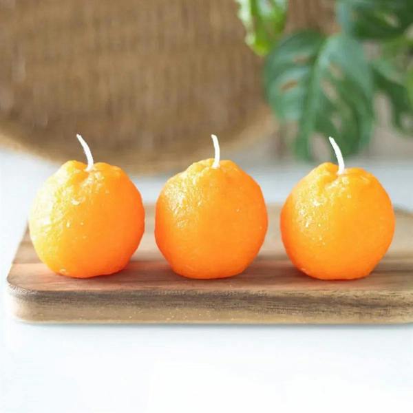 Set of three orange shaped candles with white wicks, on a wooden tray.