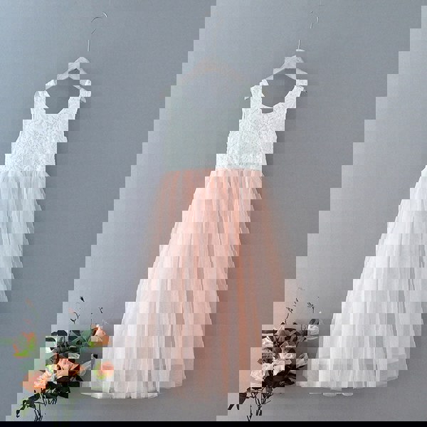 White lace top and blush tulle skirt dress on a hanger against a grey background with flowers.