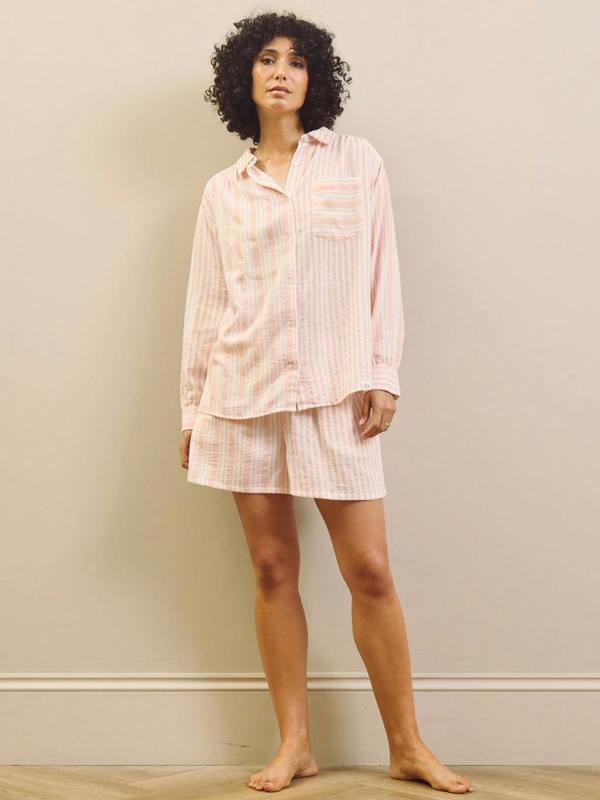 Woman wearing a pink striped short pyjama set against a plain wall.
