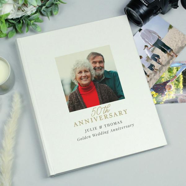 A personalised 50th Anniversary photo album featuring a golden wedding anniversary design. The cover shows a happy older couple in a square photo, with the text "50th Anniversary" and "Julie & Thomas - Golden Wedding Anniversary" printed below.