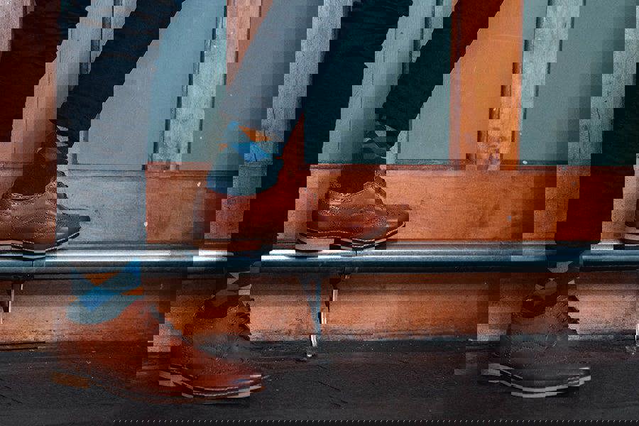 Person wearing brown shoes and dark pants with green and blue diamond pattern socks, standing on a metal bar against a wooden door.