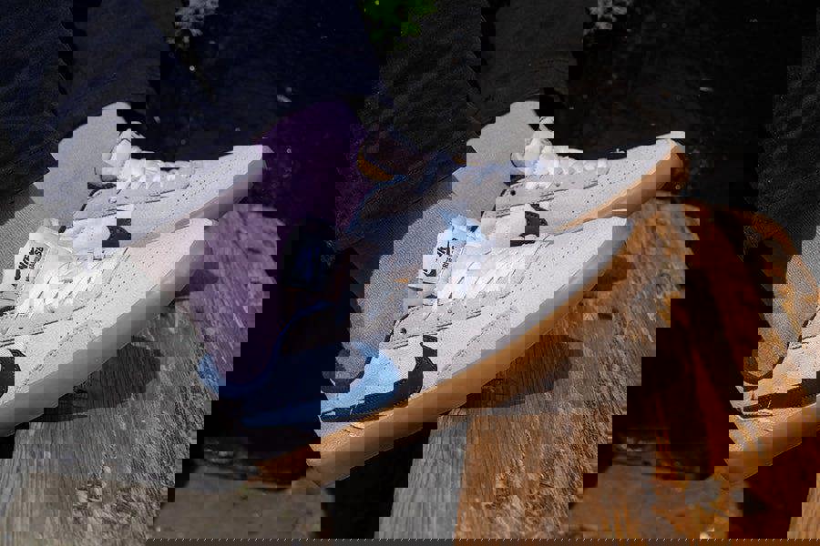 White sneakers with purple socks worn by a person sitting on a wooden bench.