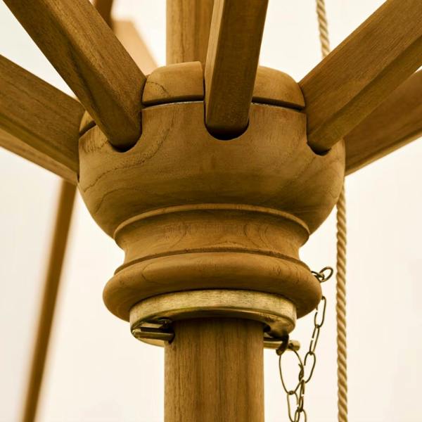 A close-up shot focusing on the brass locking pin, retaining chain, and cord mechanism under the wooden runner hub of a teak parasol.
