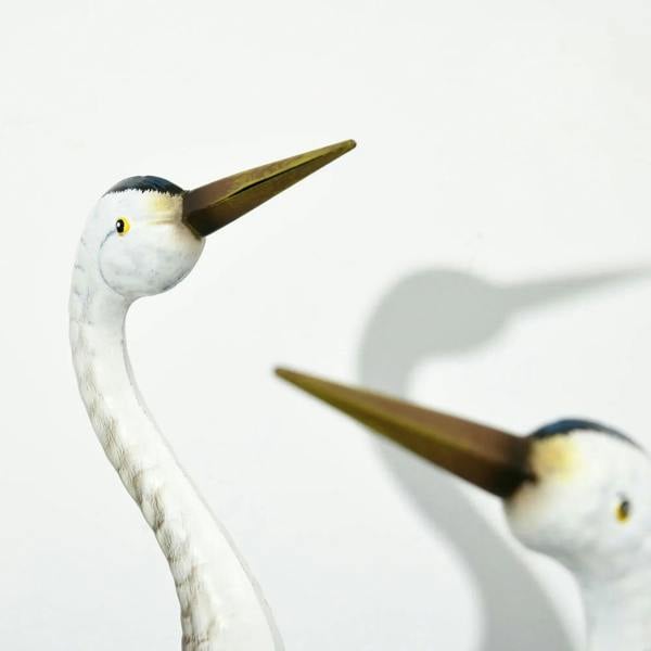 Close-up steel crane ornament with white face and long golden beak, blue feather body