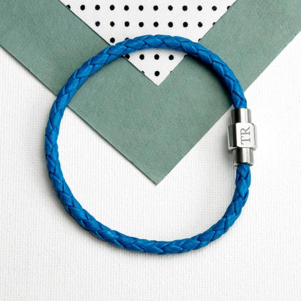 A flat-lay view of a circular cobalt blue woven leather men's bracelet with a silver metal clasp engraved with the initials TR.