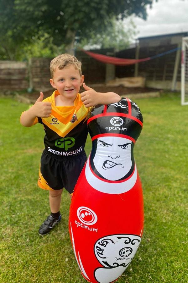 Young boy in rugby kit giving thumbs up beside a red Optimum inflatable tackle buddy in a garden - Optimum