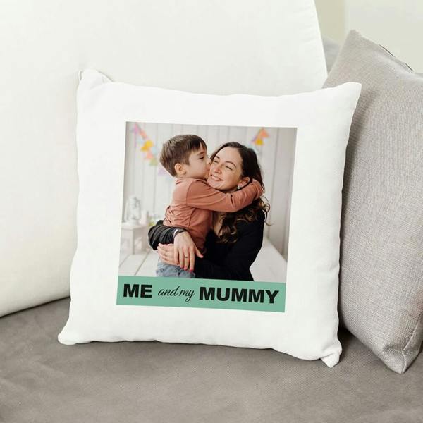 A square white cushion cover featuring a large printed photo of a happy woman (Mum) being hugged and kissed on the cheek by a young boy. Beneath the photo is a green banner with the text "ME and my MUMMY". The cushion is displayed on a grey sofa.