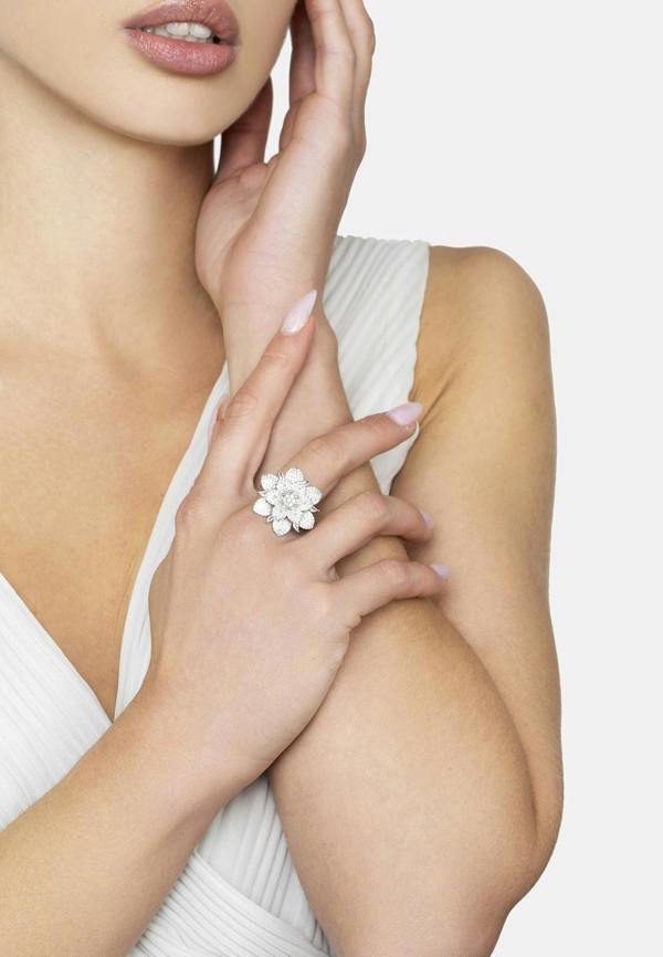 Woman wearing a white dress with a floral ring on her hand against a light background