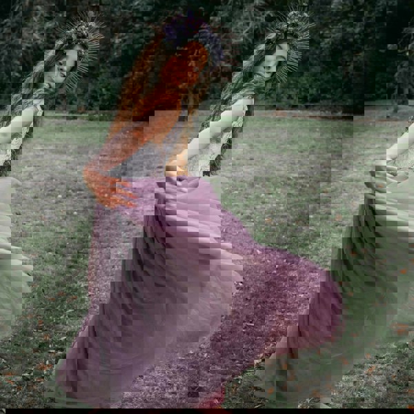 Girl in a flowing purple dress with floral headpiece standing in a grassy field.