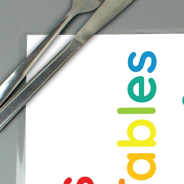 A close-up shot of a fully laminated personalised times tables placemat showing the edge seal, rainbow text, and stainless steel cutlery resting on top.