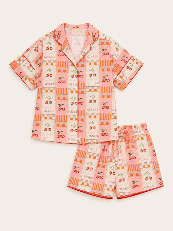 A two-piece girls' pajama set featuring a short-sleeve button-up shirt and matching shorts in a pink and orange patchwork print with cherries, hearts, stripes, and the word 'KISSES'.