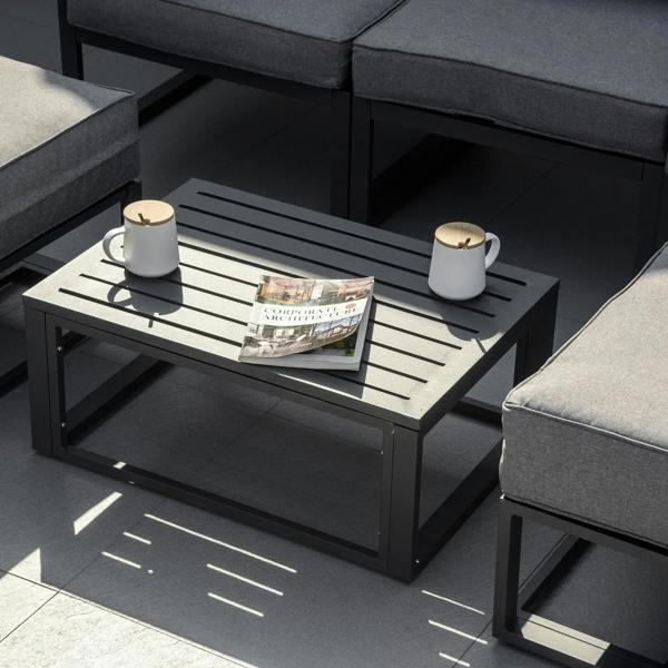 Black outdoor coffee table with slatted top beside grey cushioned ottoman seats
