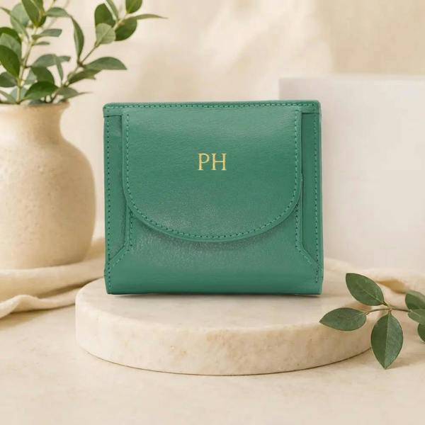 Green wallet with 'PH' initials on a marble surface with a plant in the background