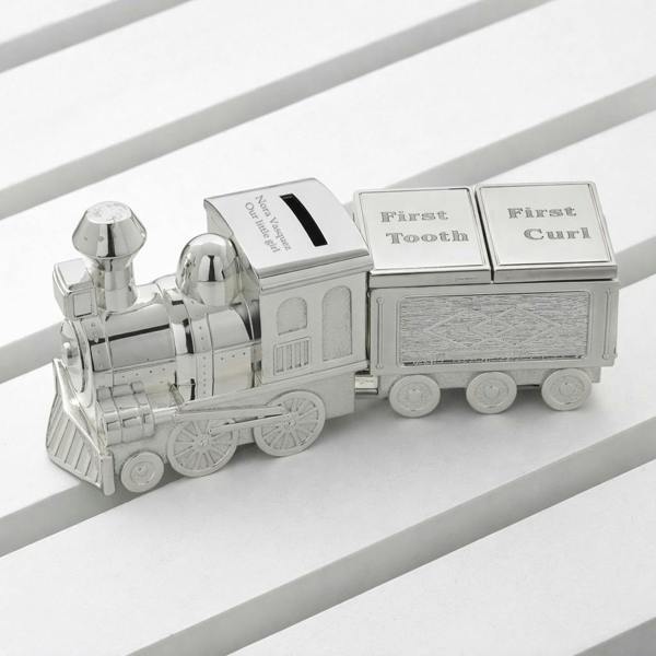 A personalised silver-plated train money box with a carriage featuring First Tooth and First Curl lids, displayed on a white slatted surface.