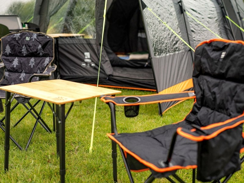 Close up Image of Henwick Padded Folding Camp Chair Orange & Black by OLPRO with the bamboo table outside a tent.