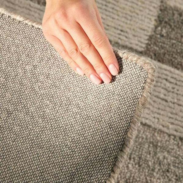Close-up of a hand touching a textured brown carpet