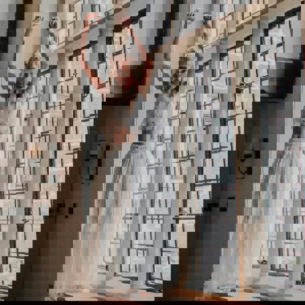 Girl in a white lace outfit standing in a room with large windows.
