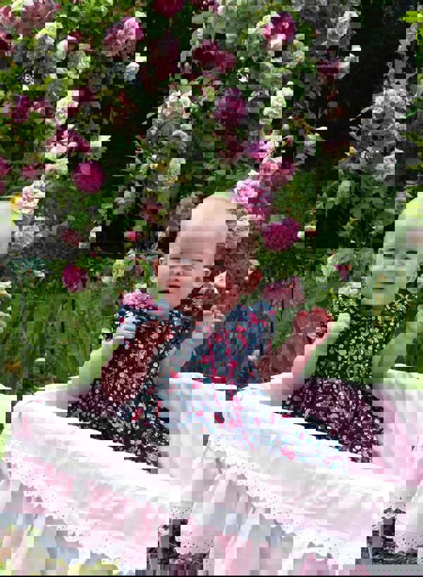 Baby in navy button-front dress with floral print, puff sleeves and pink ricrac trims and buttons.