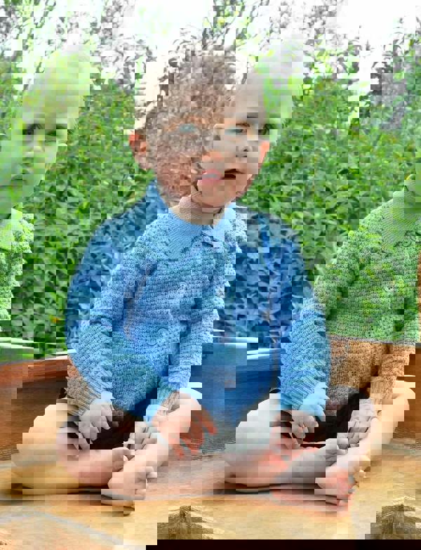 Baby boy wearing blue moss stitch cardigan, styled with navy shorts.
