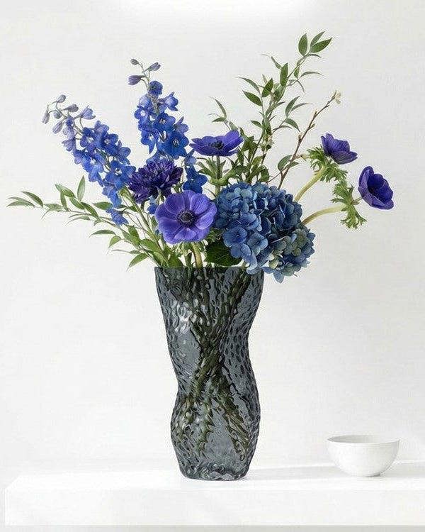 Textured gray vase with white flowers on a light surface with books in the background