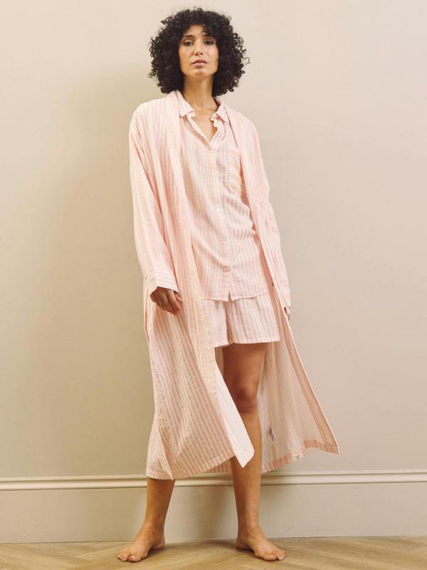 Woman wearing a pink striped pyjama set and robe against a plain background