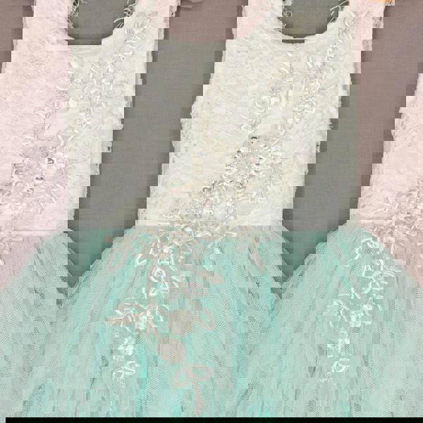 White lace top and turquoise tulle skirt dress with floral embellishments on a neutral background