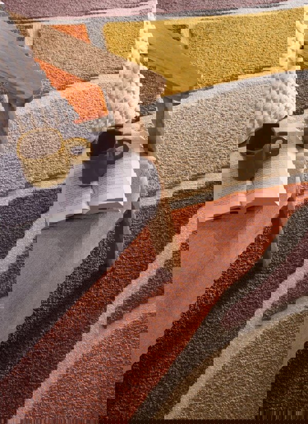 Strata Abstract Rug with deep pile in warm Terra colorway, styled near a cozy chair with a book and mug.