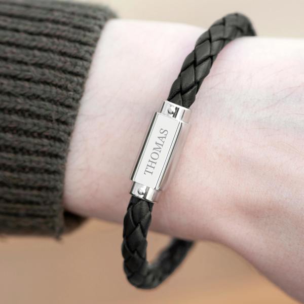 Personalised men's black braided leather bracelet worn on a wrist, featuring a stainless steel plate engraved with THOMAS